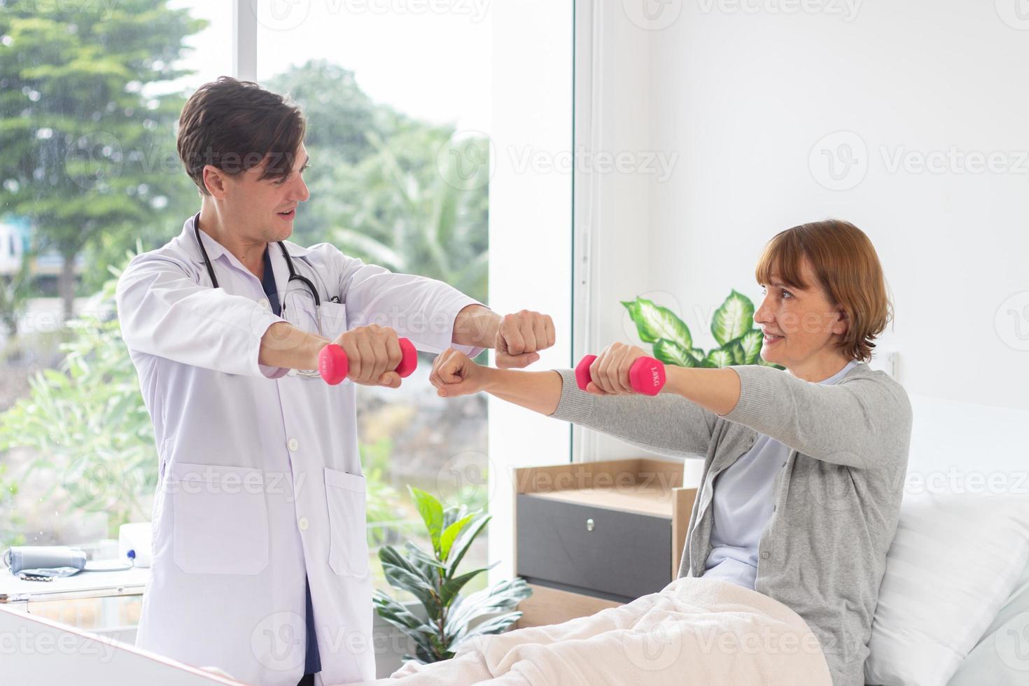 hembra paciente hacer ejercicio con pesas en el hospital. fisioterapeuta ayudando mayor mujer a levantar mancuernas el médico es examinando el paciente en el hospital foto