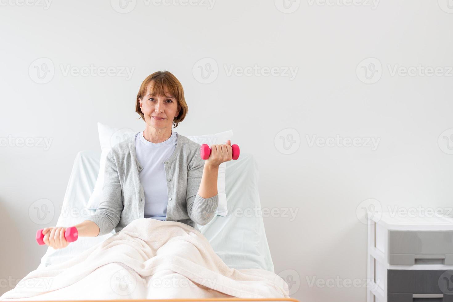 hembra paciente hacer ejercicio con pesas en el hospital. fisioterapeuta ayudando mayor mujer a levantar mancuernas el médico es examinando el paciente en el hospital foto