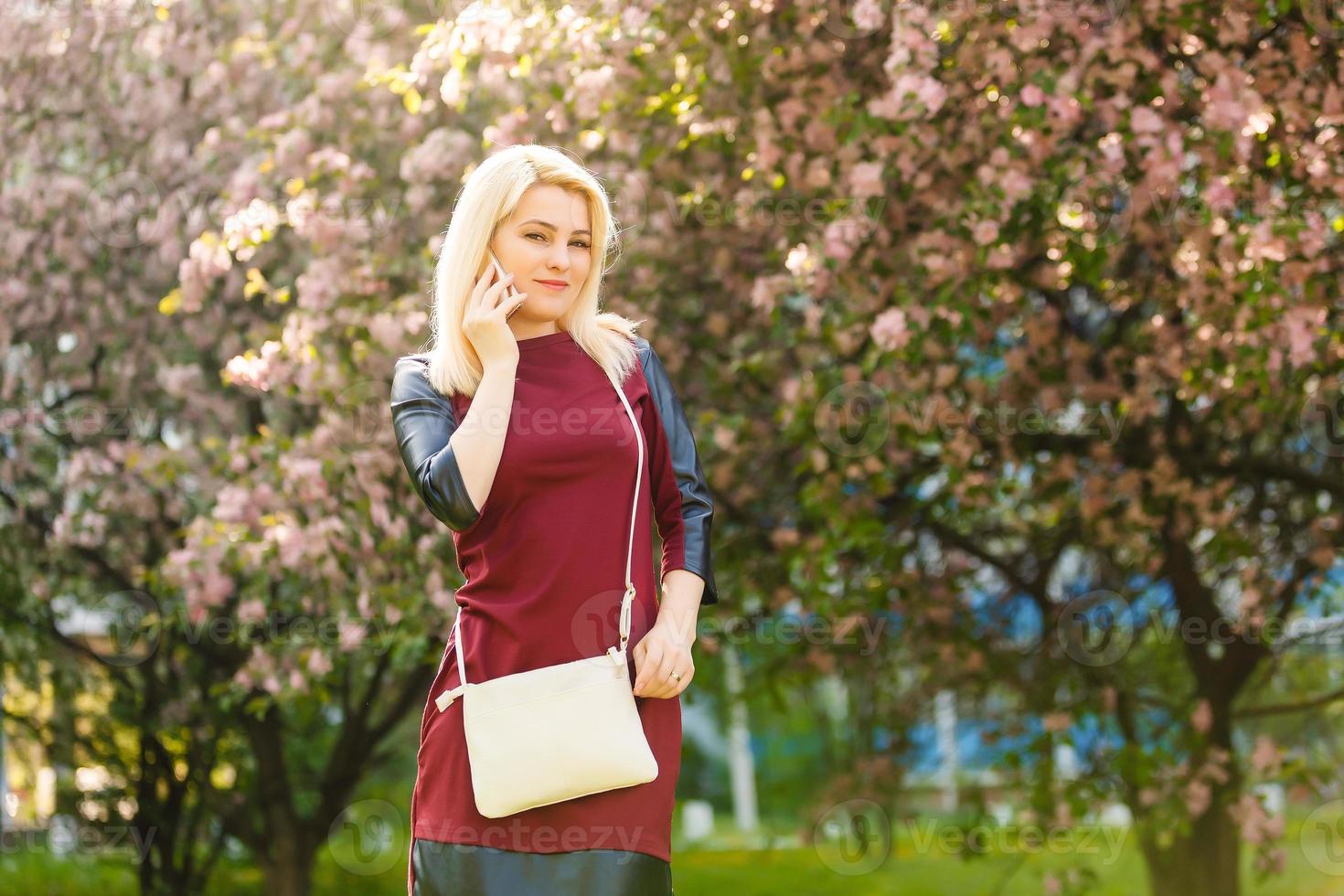 Woman with gorgeous smile having fun in blooming garden. Female with slim sexy body on natural background, wellness and fitness concept. Sensual blond girl in short chiffon dress walking in park. photo