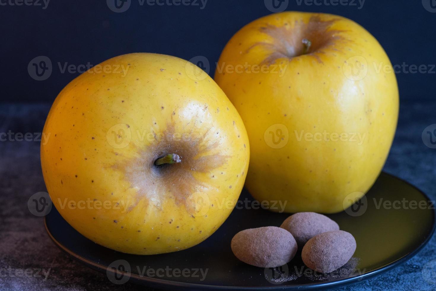 Two opal apples and three chocolate-covered almonds on a black plate. photo