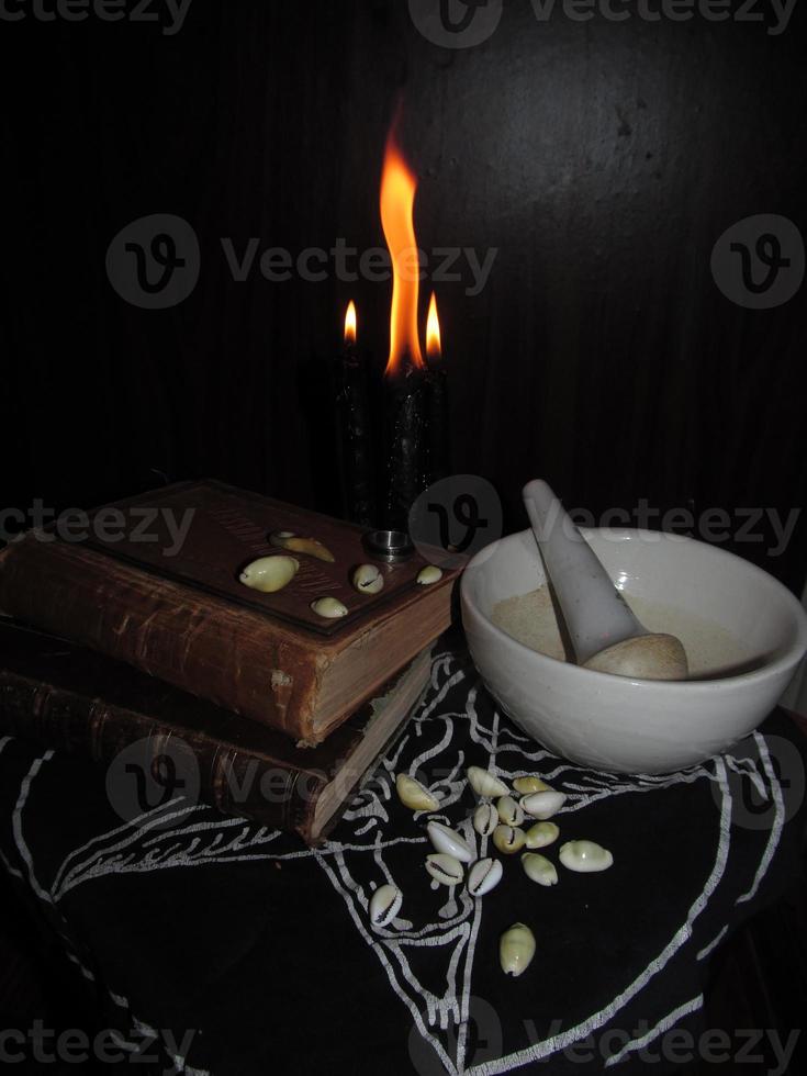 negro magia ritual todavía vida. negro velas, libros, cauri conchas, mortero y majadero, un anillo en un oscuro antecedentes foto