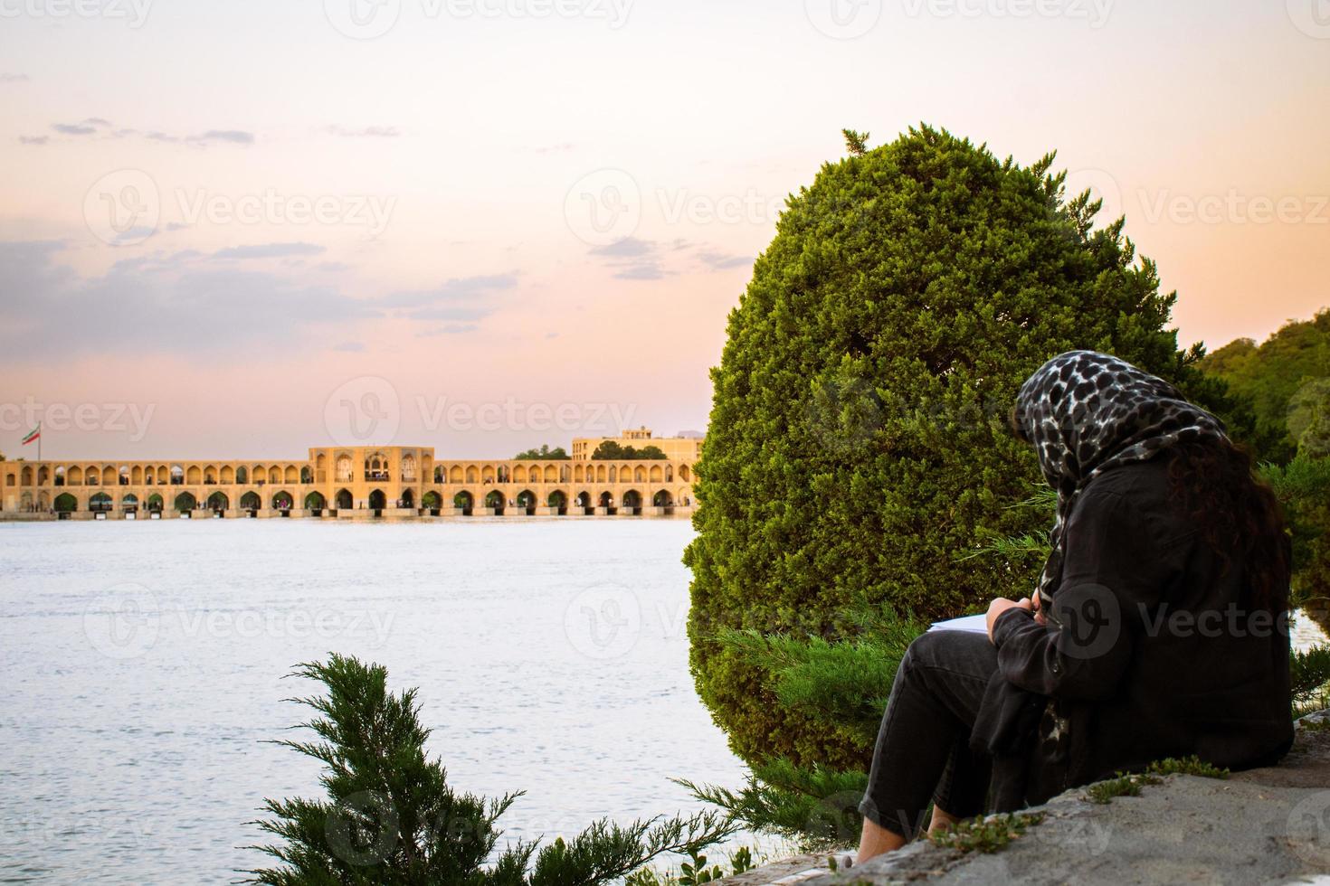 isfahán, corrí - mayo 2022, musulmán estudiante sentar con libro estudiar fuera de por siose pol o puente de 33 arcos, uno de el más antiguo puentes de esfahan y mas largo puente en zayandeh río foto