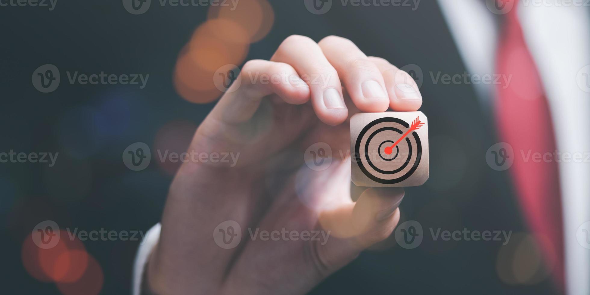 Wooden block in businessman hand and arrow icon hitting center of dartboard target,Setting business goals and focused concepts, Organizational growth and objectives, marketing strategy planning photo