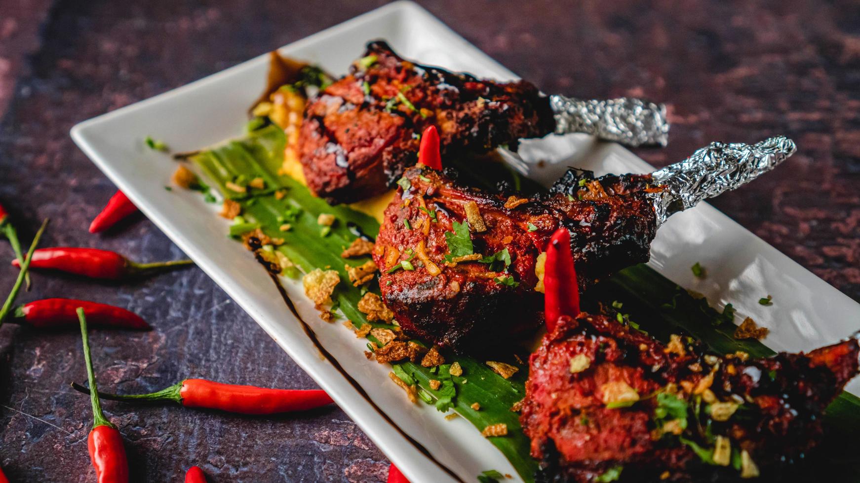 frito pollo pirulí con picante salsa y frito ajo. suelo rojo carne, en un puntiagudo tribal estilo, estaño frustrando servido en un plato y plátano hoja con rojo especias alrededor. foto