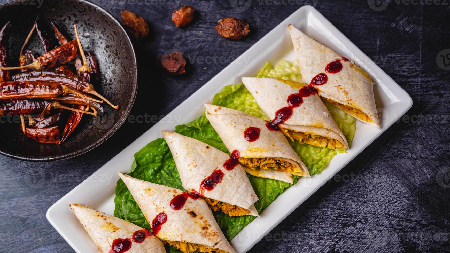 Royal Indian kathi rolls with spicy sauce and lettuce on a white plate., chilies on the side photo