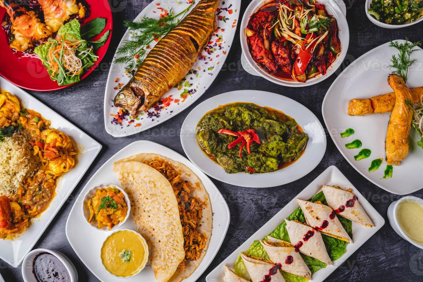 Nawabi Indian curry dishes with grilled fish, spicy chicken curry, paratha bajhi, prawn curry, biriyani, rolls, tomato, and green curry. photo