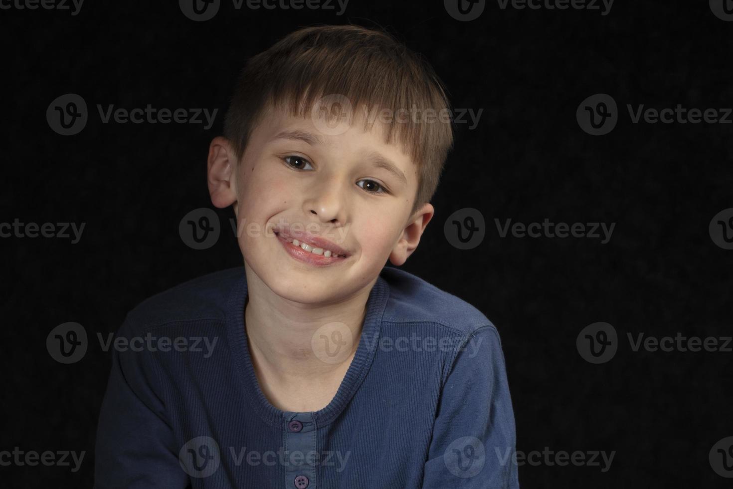 Portrait of a ten-year-old boy on a dark background. The child looks into the camera with intelligent eyes. Handsome boy of school age. photo