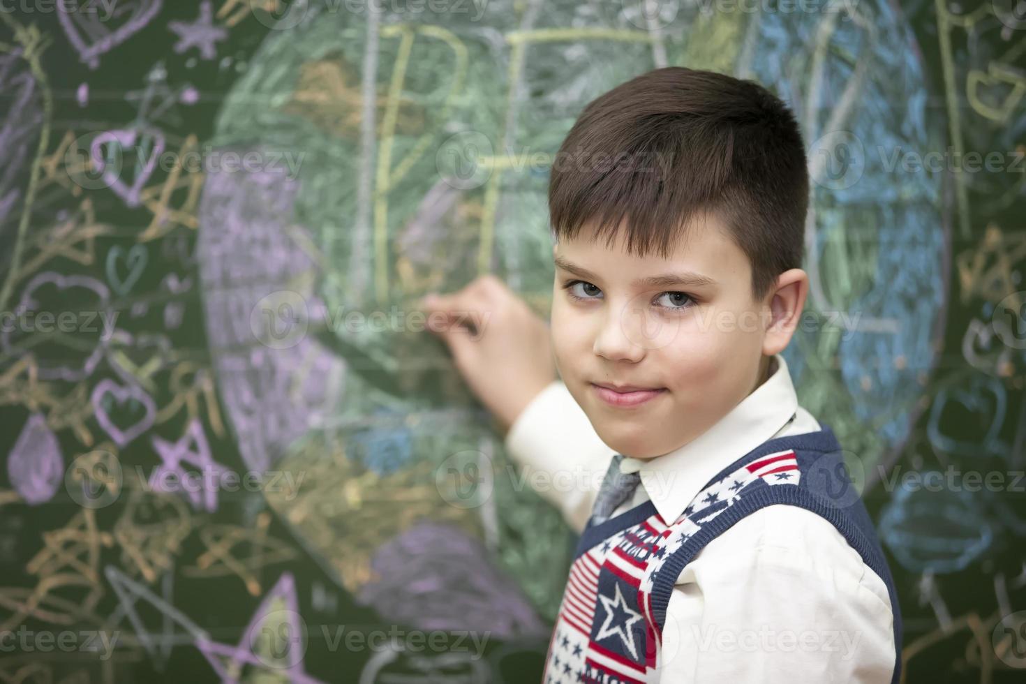 The schoolboy at the blackboard draws with chalk. Middle school age. The boy is in the classroom. photo