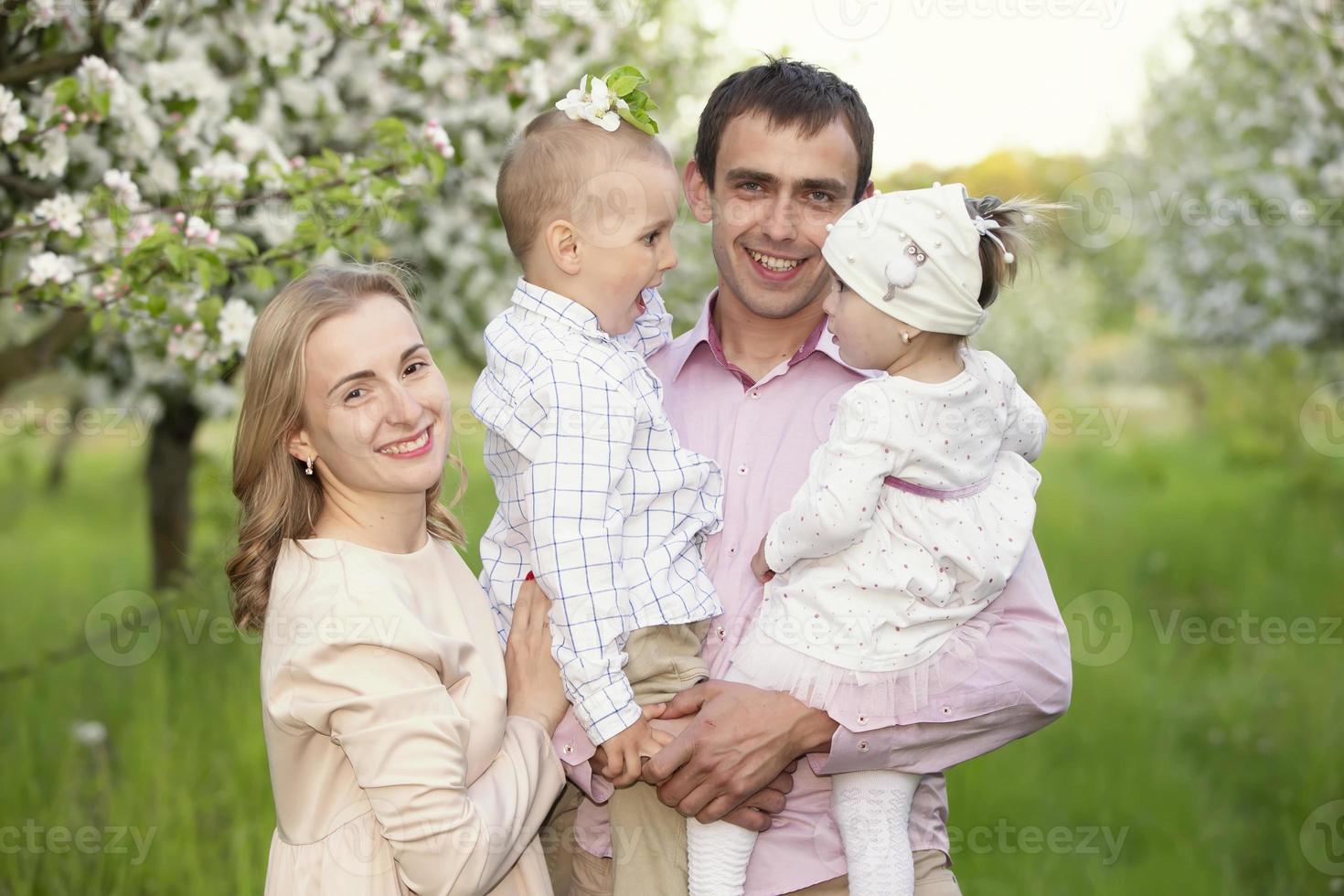 contento padres mamá y papá, hija y hijo, joven familia al aire libre en primavera en contra el fondo de floreciente manzana y Cereza arboles foto