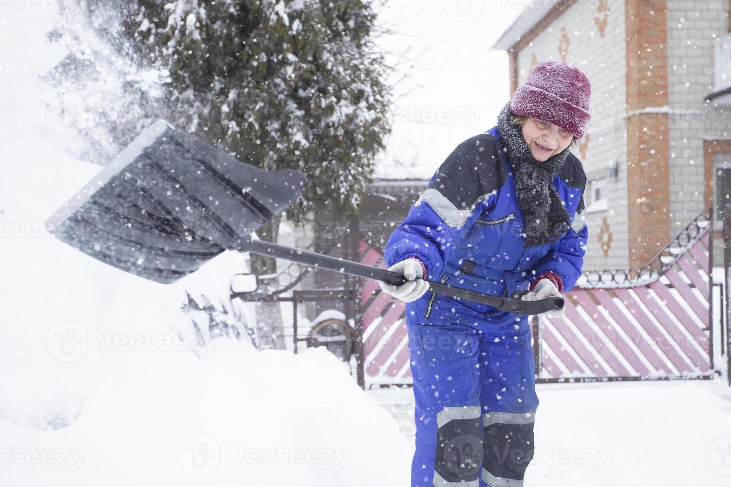 Shoveling snow near the house. An elderly woman clears the road after a snow storm. photo