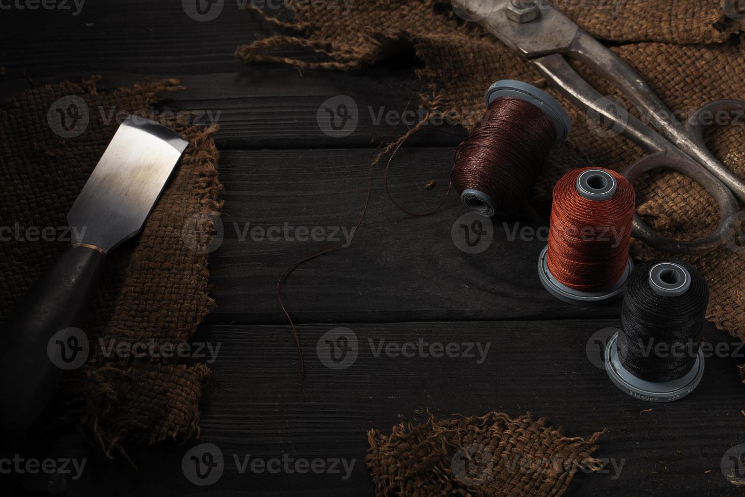 en un oscuro fondo, de coser hilos, un parte de hierro tijeras y un herramienta para de coser cuero. foto