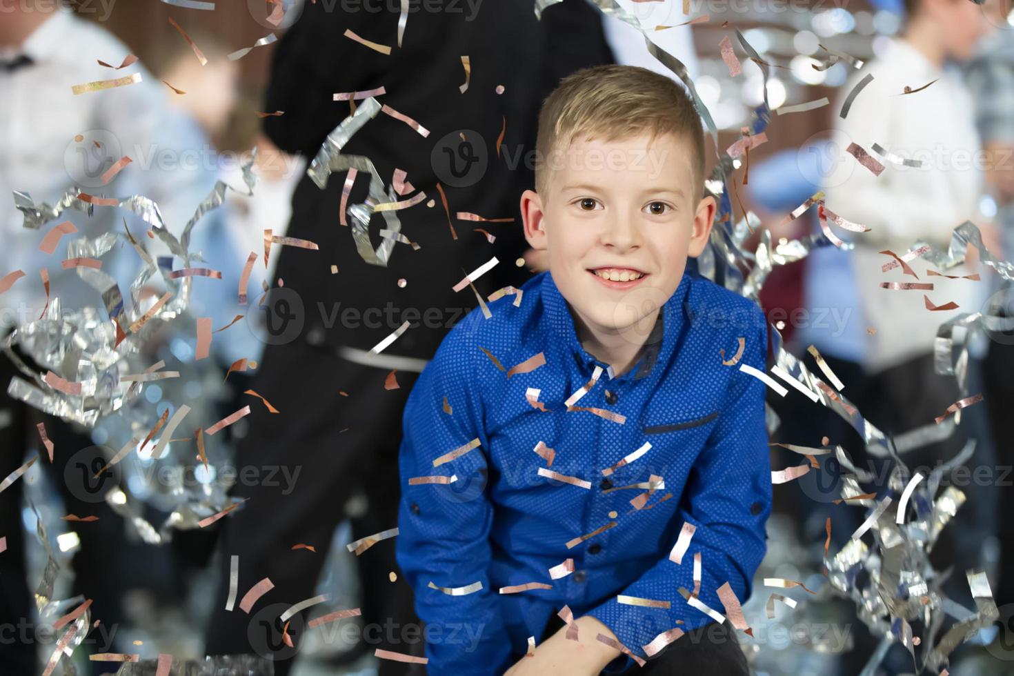 Happy little boy in confetti.Magic time - Portrait of a very happy child with hands smiling while falling confetti. At a children's party. photo