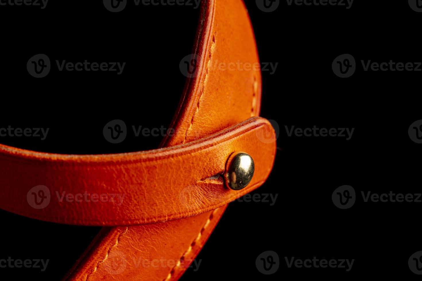Part of a leather product or belt with a metal rivet on a black background. photo