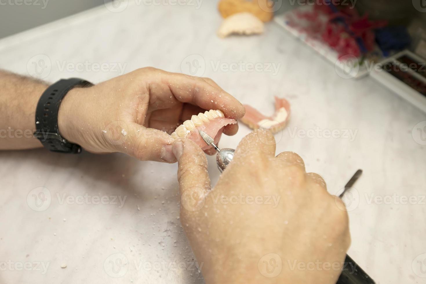 Manufacturing of dentures. Orthopedist's hands make jaw prostheses. photo