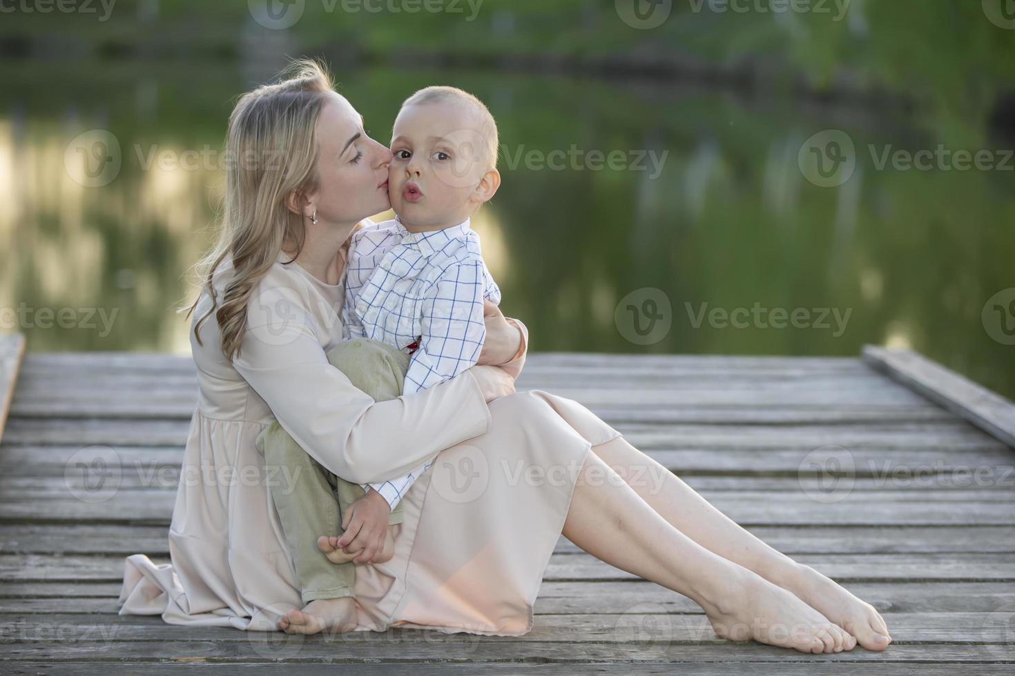 mamá suavemente Besos su pequeño hijo en contra el fondo de naturaleza. materno felicidad. foto