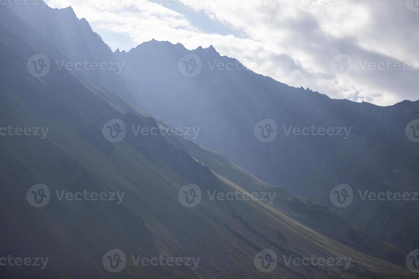 Dark atmospheric surreal landscape with a dark rocky mountain peak in low clouds in a gray cloudy sky. A gray low cloud on a high peak. High black rock in low clouds. Surreal gloomy mountains. photo