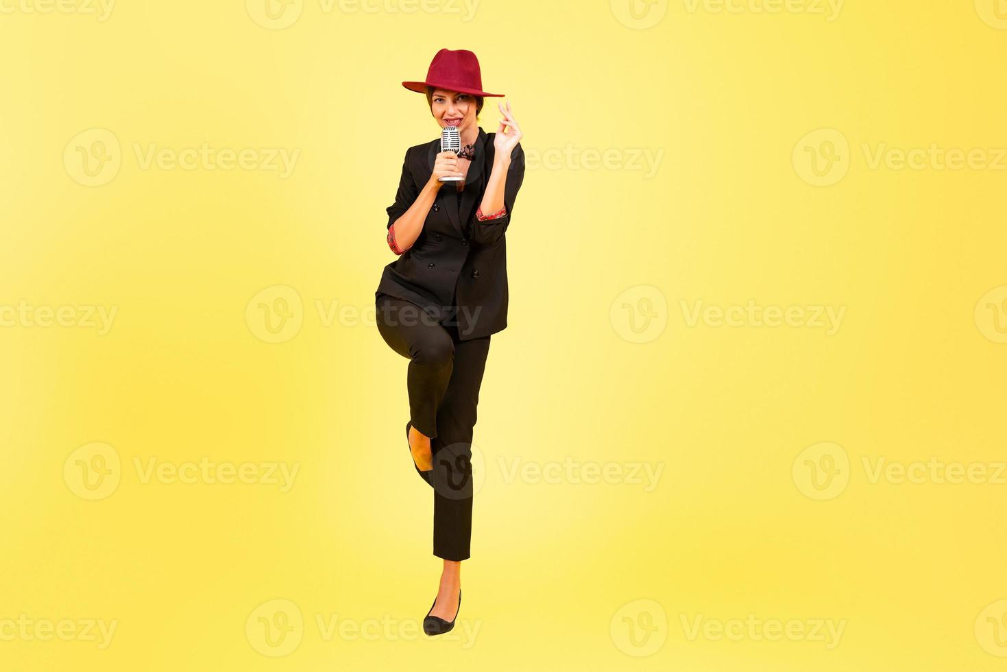 girl in a black suit on a yellow background sings in a retro microphone, portrait, music, full growth photo