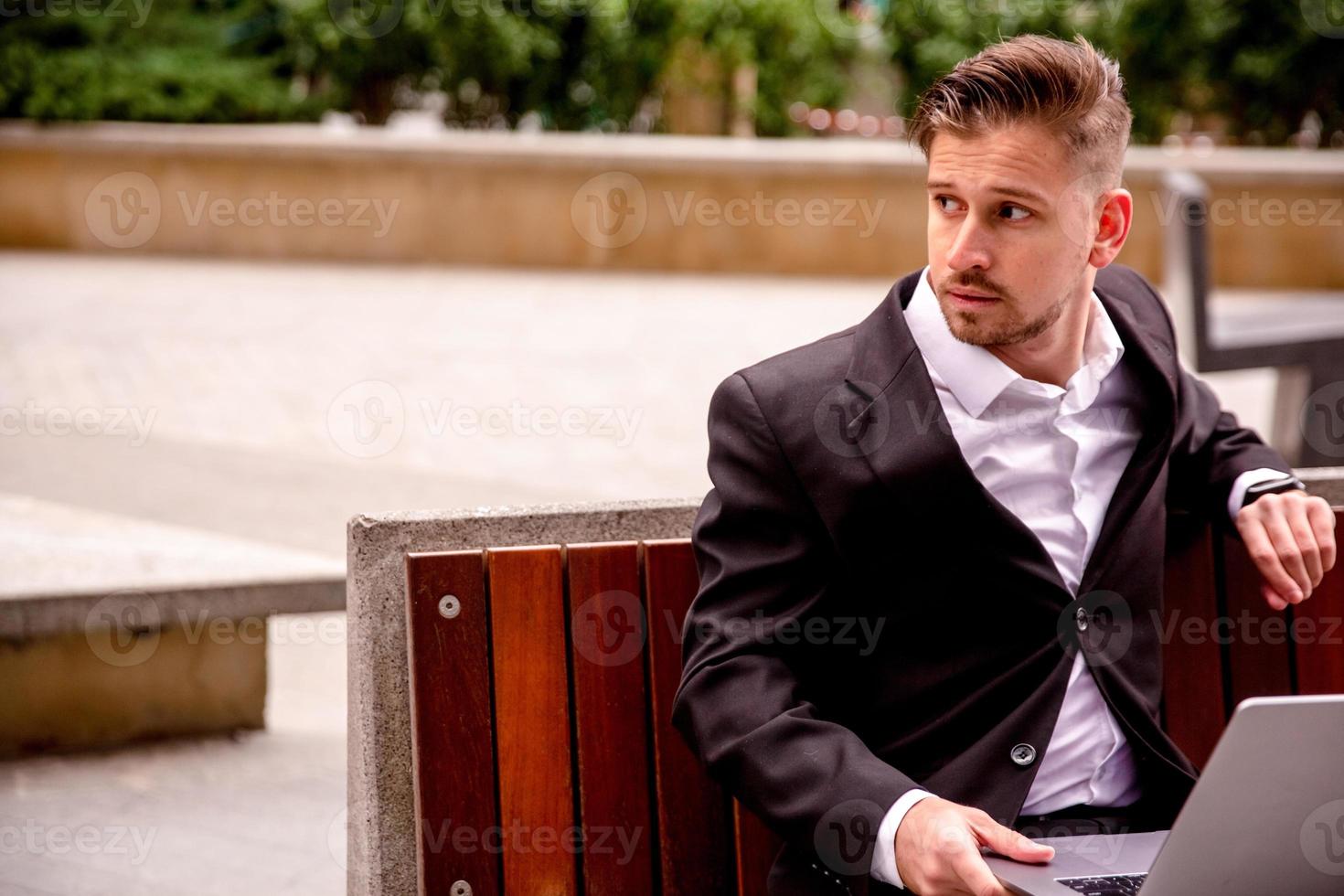 Young guy in a suit works on a computer in the park of a business center photo