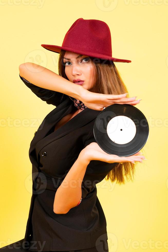 girl in a black suit on a yellow background with a record in her hands, music, the girl shows emotions photo