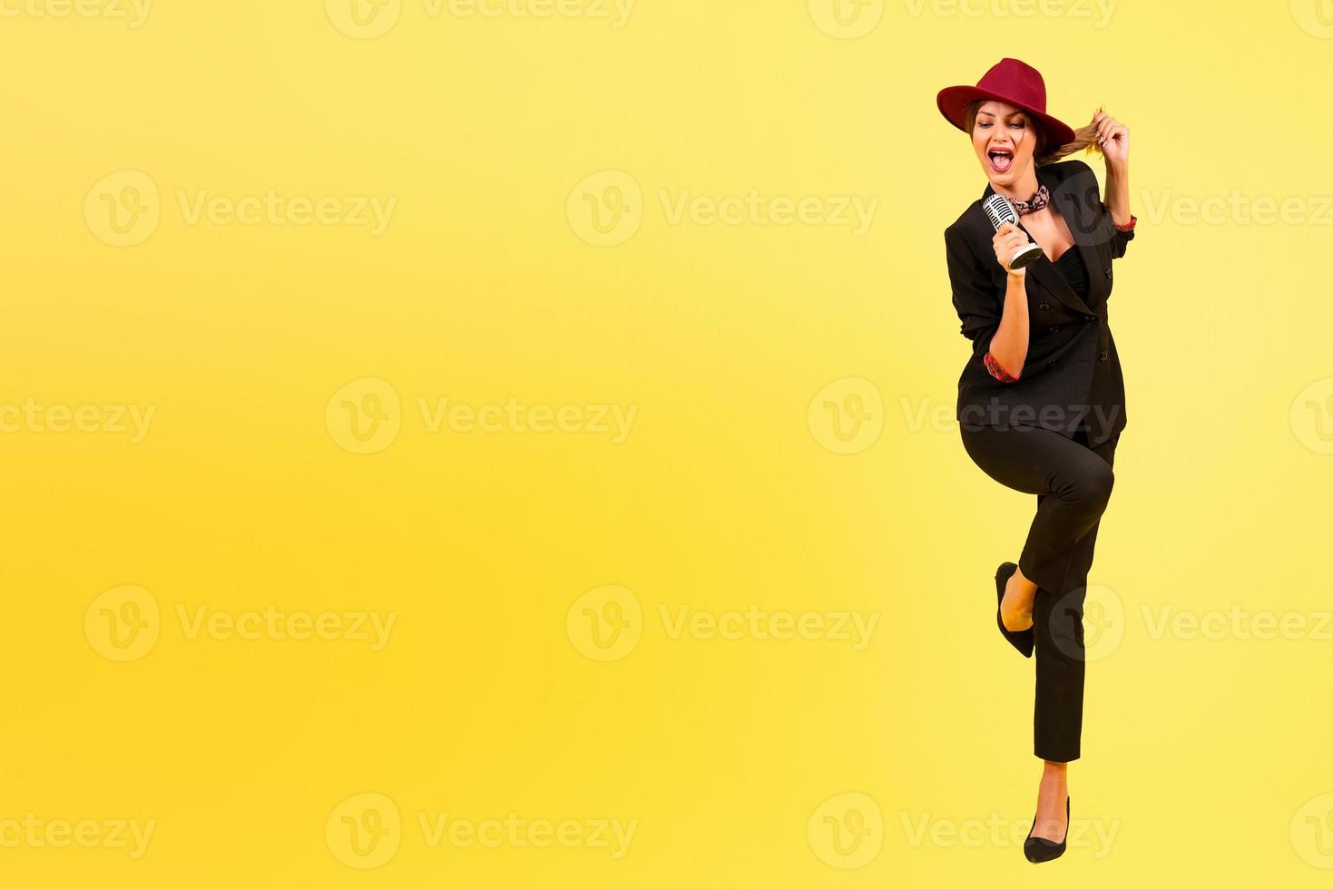 girl in a black suit on a yellow background sings in a retro microphone, portrait, music, full growth photo