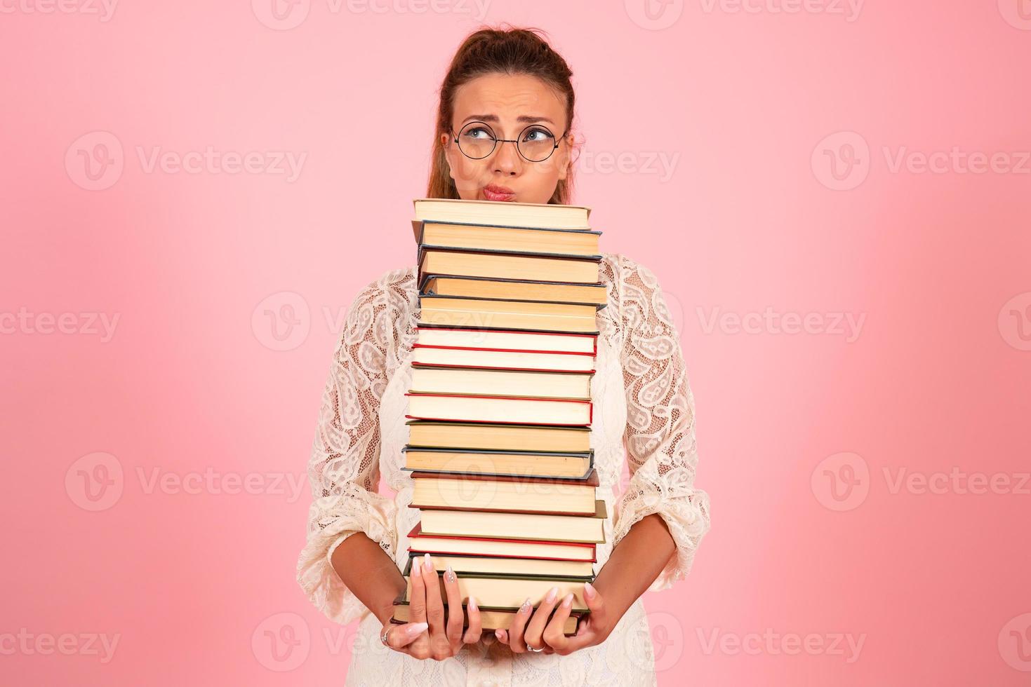 Pink background, girl reading books, book lover, student holding a large stack of books photo