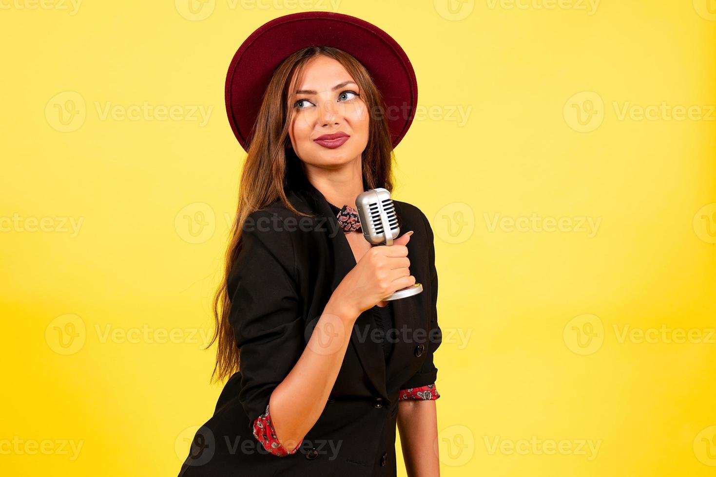 girl in a black suit on a yellow background sings in a retro microphone, portrait, music photo
