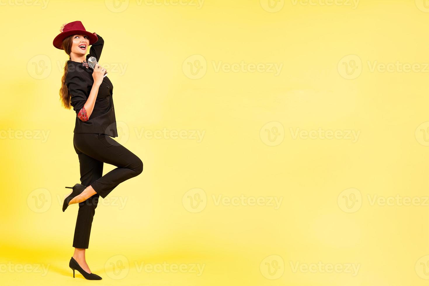 girl in a black suit on a yellow background sings in a retro microphone, portrait, music, full growth photo