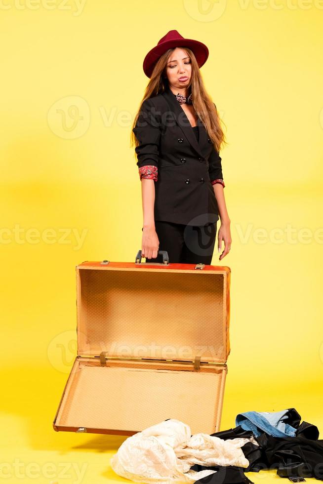 niña en un negro traje en un amarillo con un maleta en su manos un viajero foto