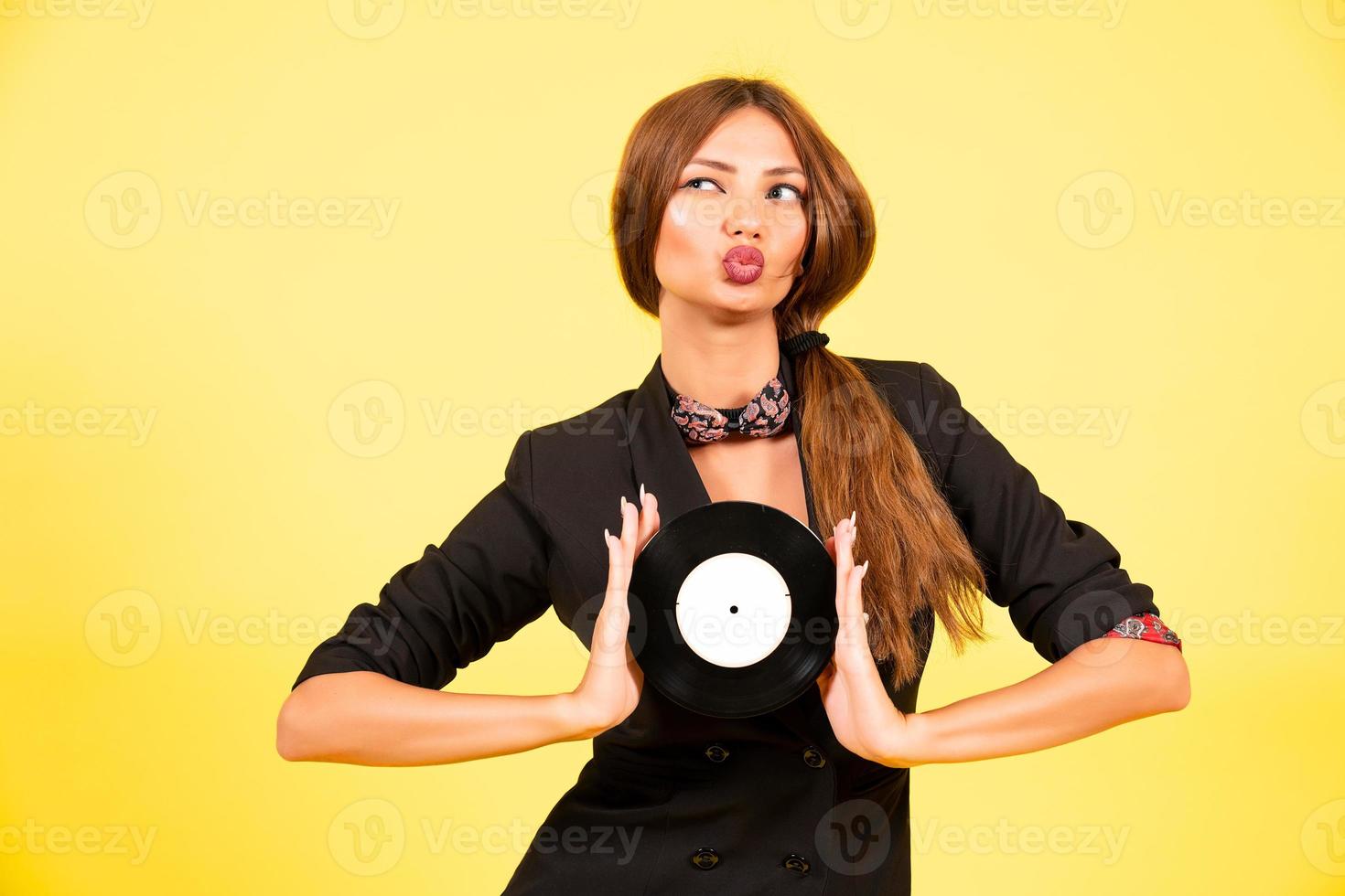 girl in a black suit on a yellow background with a record in her hands, music, the girl shows emotions photo