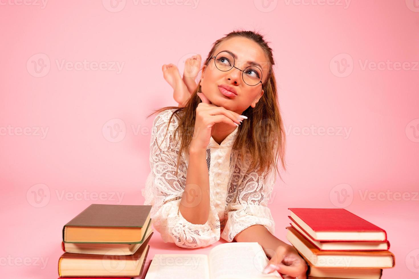 Pink background, a girl reads books, a book lover, a student lies on the floor among a large number of books photo