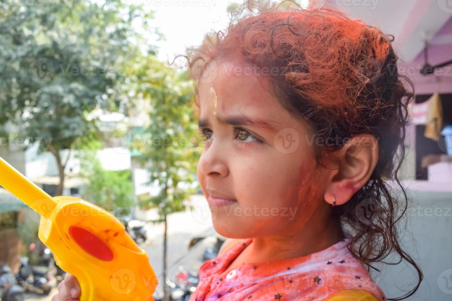 dulce pequeño indio niña jugando colores en holi festival, participación pichakaree lleno de colores, holi festival celebraciones en Delhi, India foto