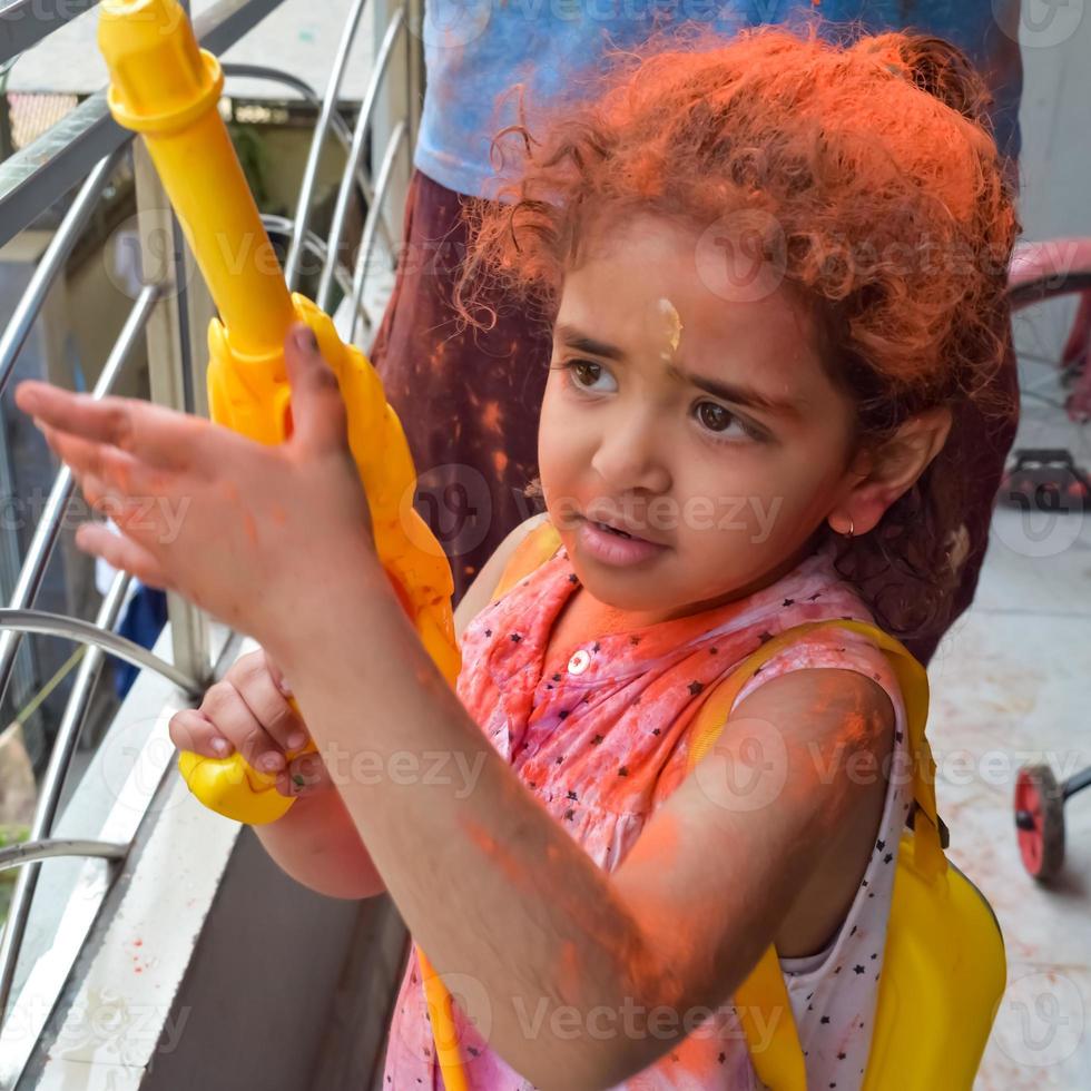 dulce pequeño indio niña jugando colores en holi festival, participación pichakaree lleno de colores, holi festival celebraciones en Delhi, India foto