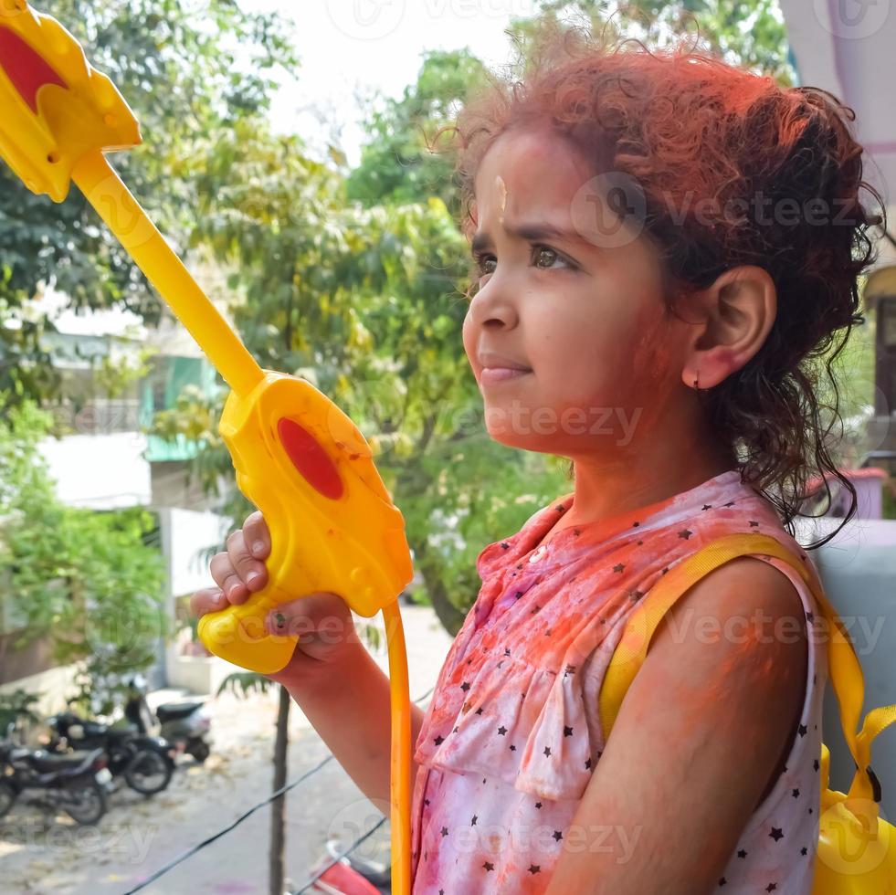 dulce pequeño indio niña jugando colores en holi festival, participación pichakaree lleno de colores, holi festival celebraciones en Delhi, India foto