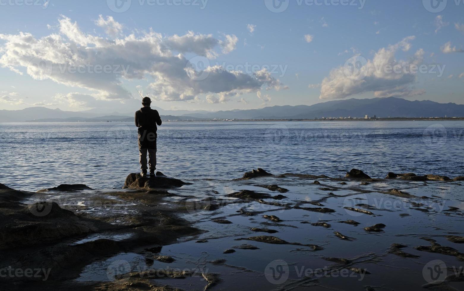 paisaje espectacular en la costa de enoshima, japón, con un pescador solitario parado al borde del agua foto