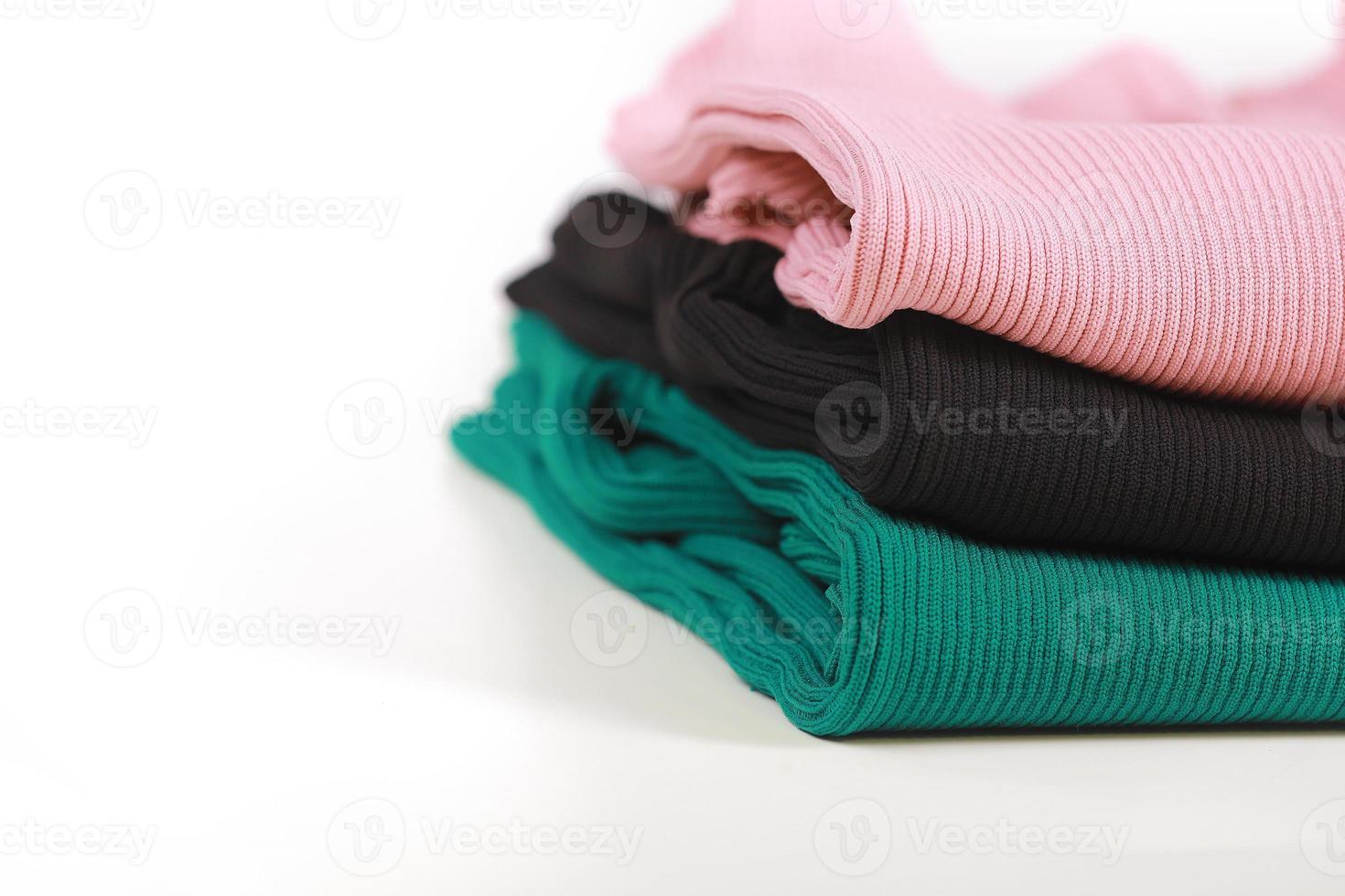 Pile of knitted warm colorfull sweaters with different knitting patterns folded in stack on white background, white wall background. Fall winter season knitwear. Close up, copy space for text photo
