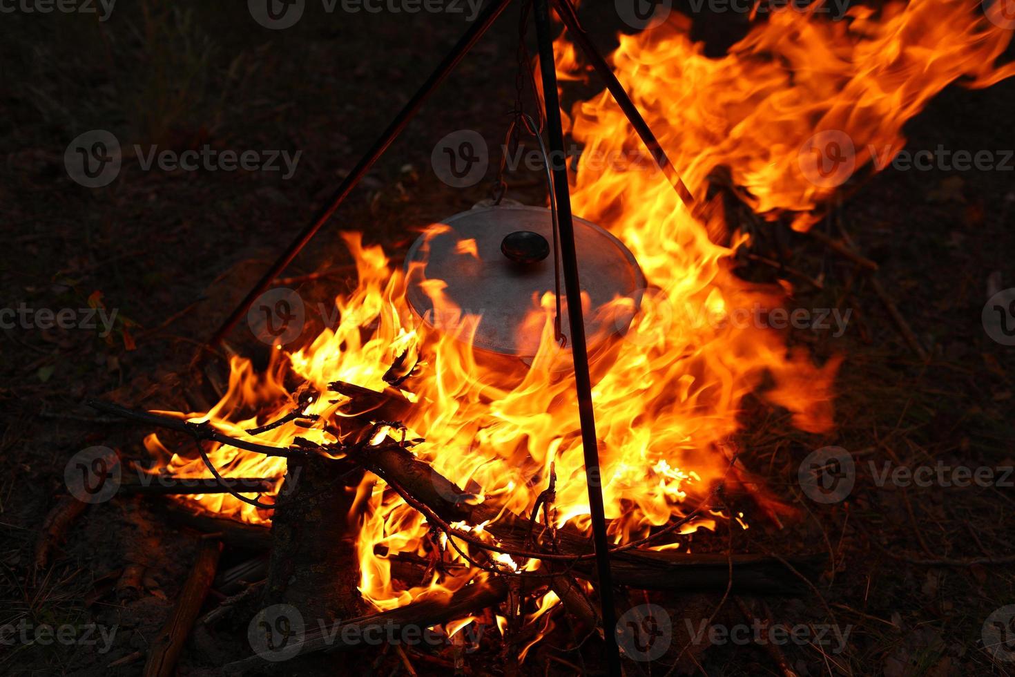 Cooking outdoors in field conditions. Cauldron on a fire in the forest. Cooking at the stake while traveling. Tripod with a bowler hat on a fire on picnic. Conceptual travel, trekking and adventure photo