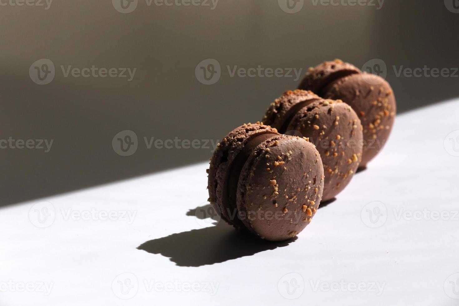 Sweet brown chocolate french macaroons or macarons dessert isolated on white background with light rays from window. copy space. photo