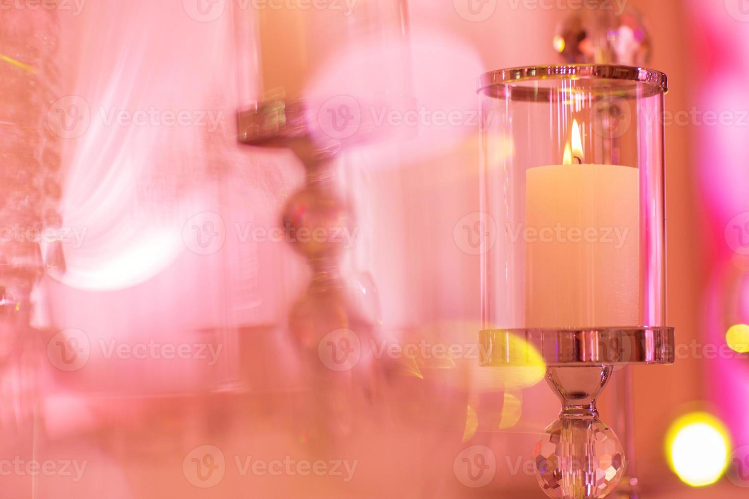 mesa de boda festiva con velas encendidas y cristal en luz rosa. portavelas de cristal como pieza central en la recepción de una boda. foto