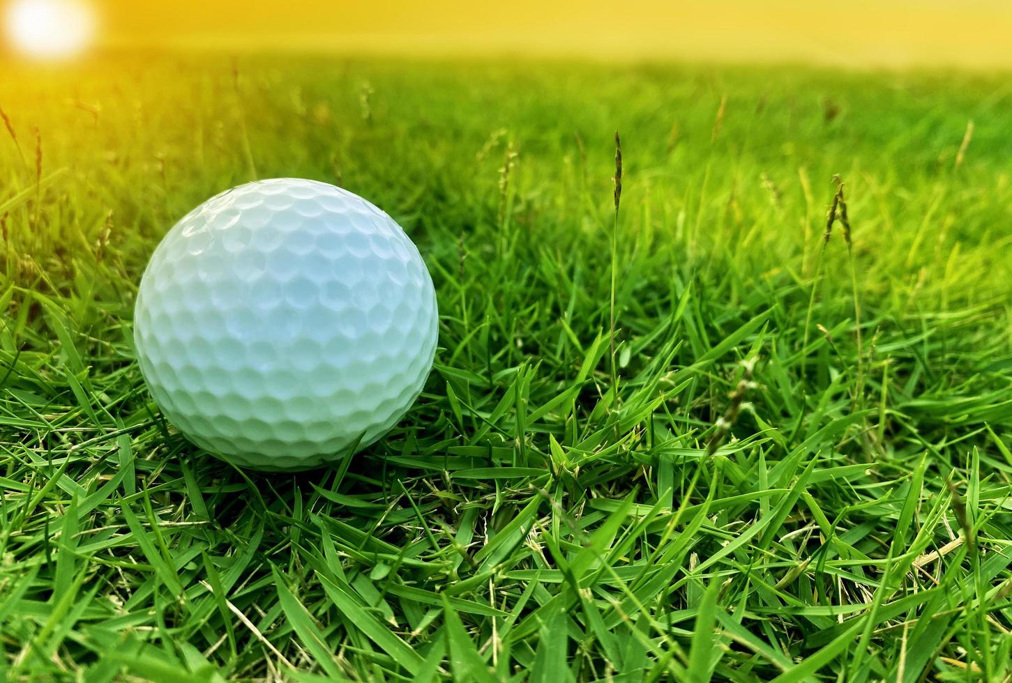 pelota de golf cerca de la hierba verde en el hermoso paisaje borroso del campo de golf con amanecer, atardecer en segundo plano. concepto de deporte internacional que se basa en habilidades de precisión para la relajación de la salud. foto