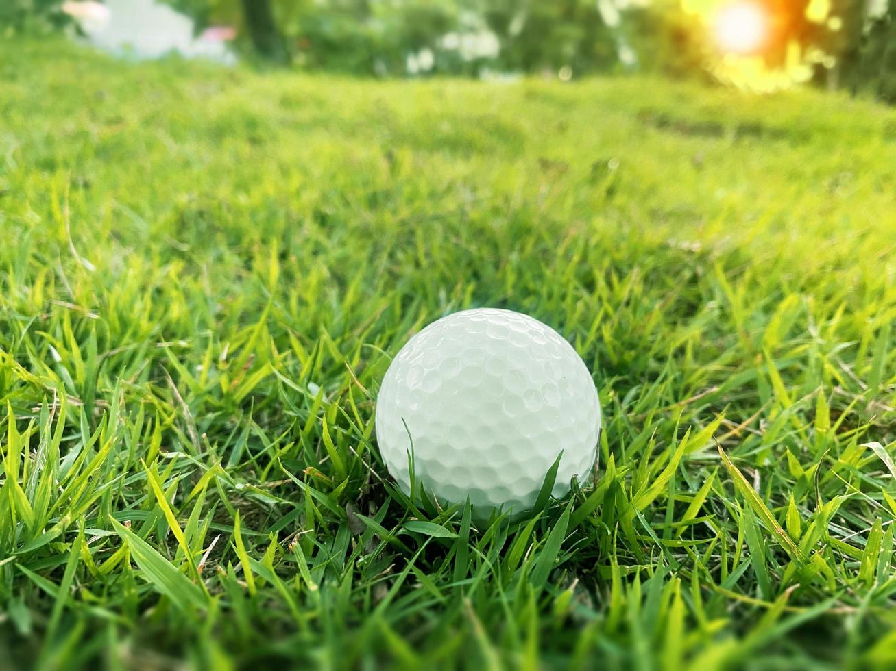 pelota de golf cerca de la hierba verde en el hermoso paisaje borroso del campo de golf con amanecer, atardecer en segundo plano. concepto de deporte internacional que se basa en habilidades de precisión para la relajación de la salud. foto