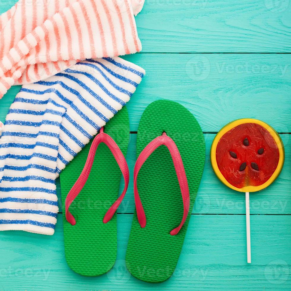 accesorios de verano. chanclas, gafas de sol, toalla, gorra roja y naranjas sobre fondo de madera azul. copie el espacio. foto