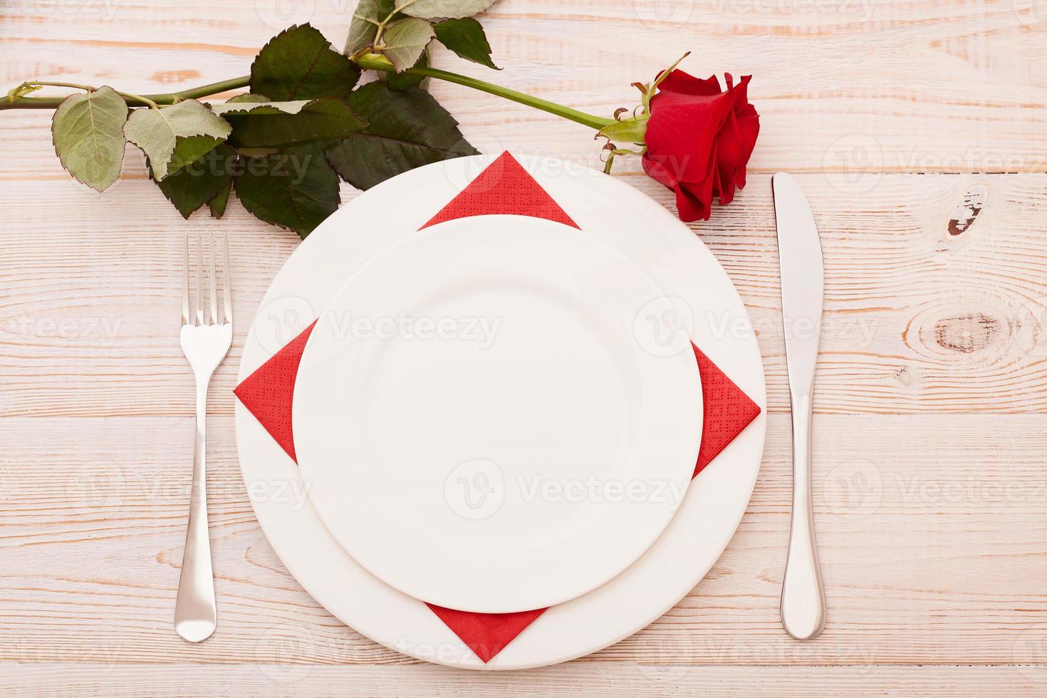 Top view of tableware of round and heart shaped empty plate, metal knife and fork served on white wooden table with glowing candle and gift box prepared for celebration of saint valentine day photo