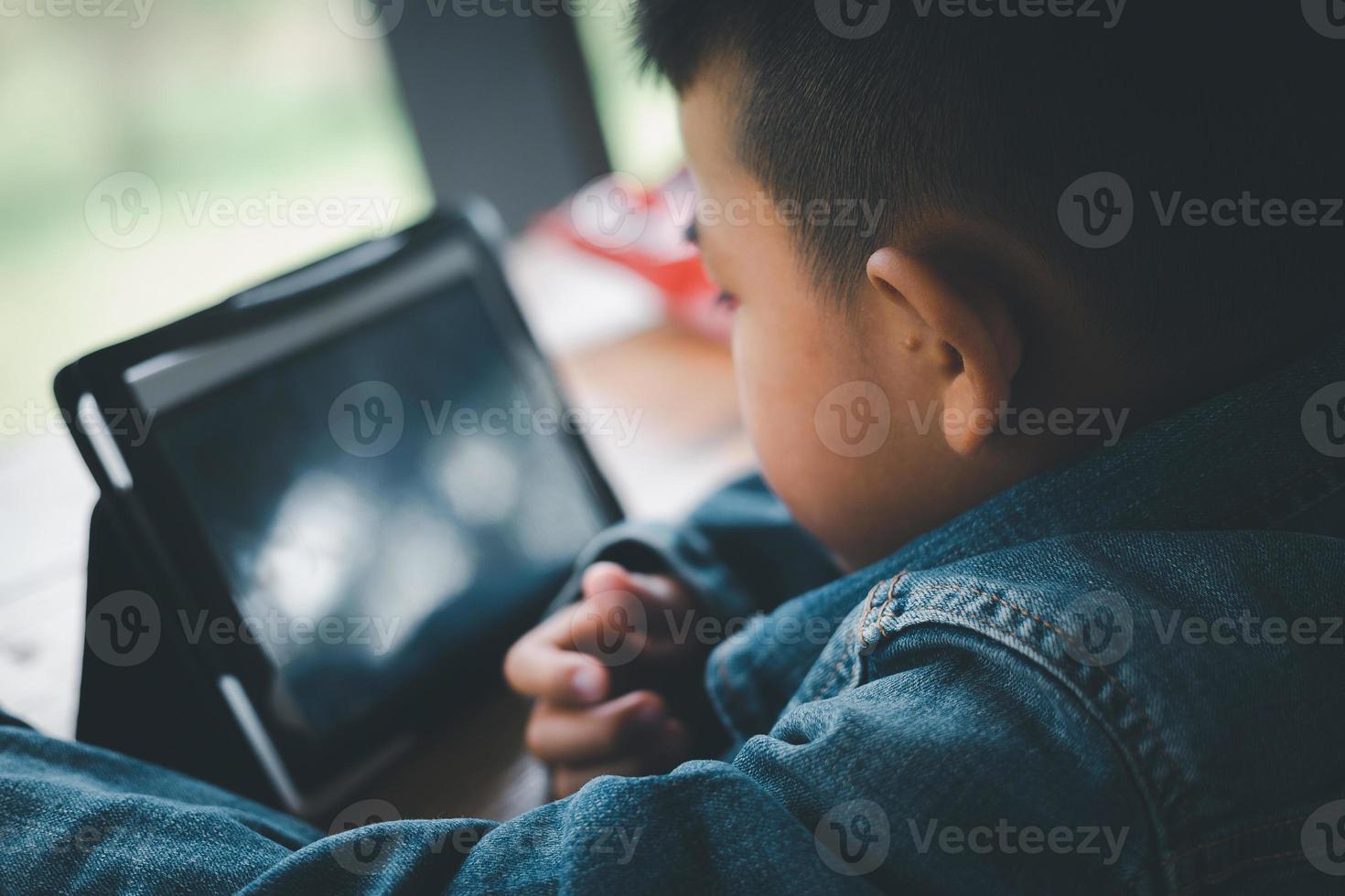 Asian boy looking at the tablet screen attentively. overstimulated children concept. Too much screen time. 5 years boy watching videos. Internet addiction concept. photo