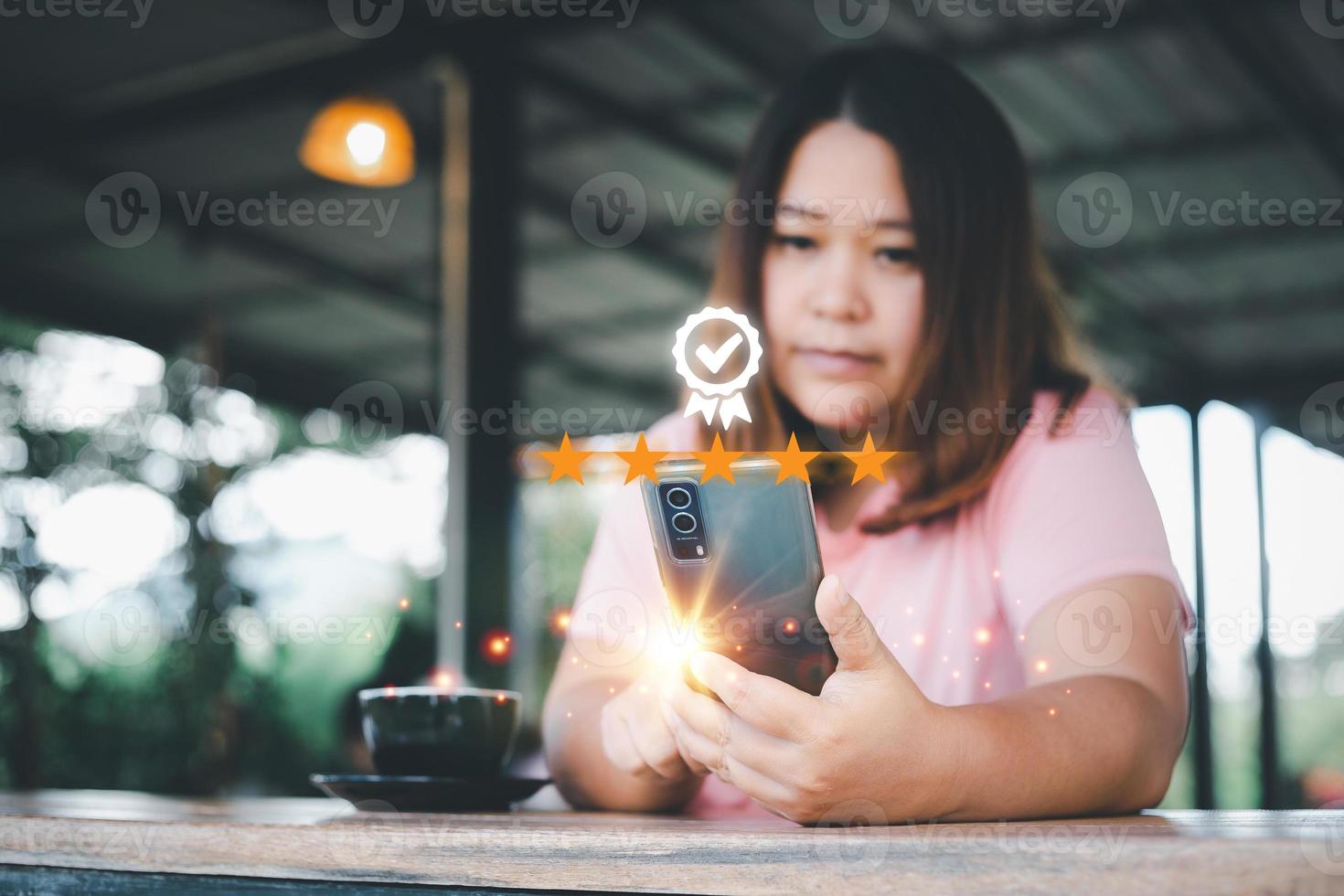 cliente experiencia concepto. asiático mujer utilizando un teléfono inteligente sentado en un café tienda demostración un excelente cinco estrellas clasificación. foto