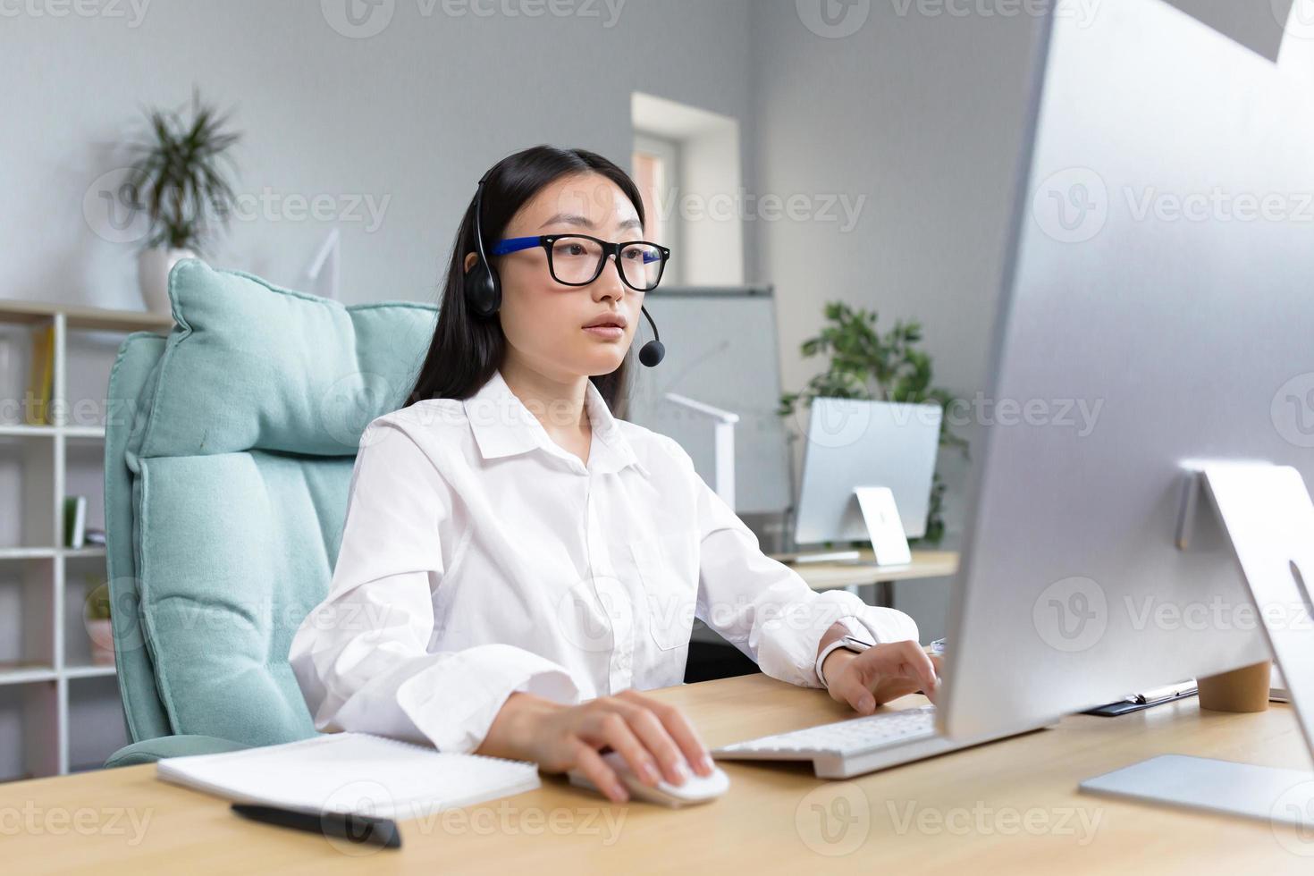 Online distance learning. Asian teacher in headphones sitting at a table teaching a lesson online photo