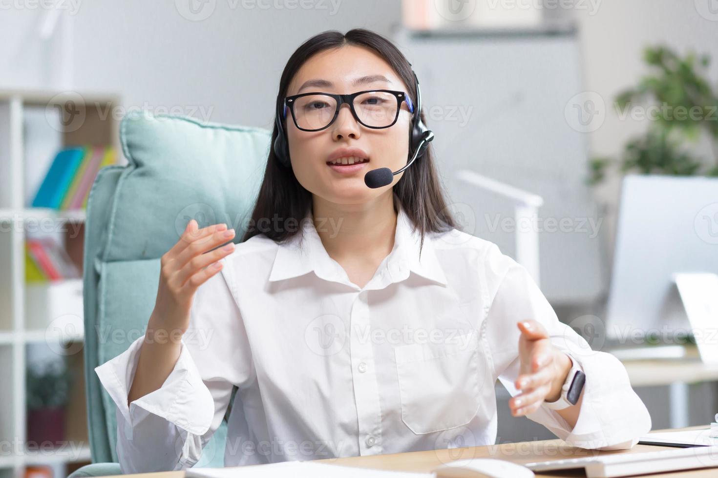 Online distance learning. Young beautiful Asian female teacher in headphones and glasses photo