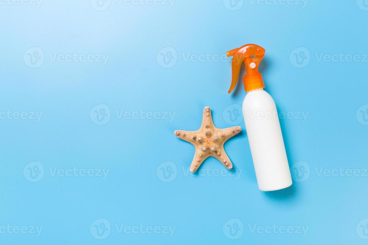 sunscreen cream with starfish and seashells in bottles on blue background, top view photo