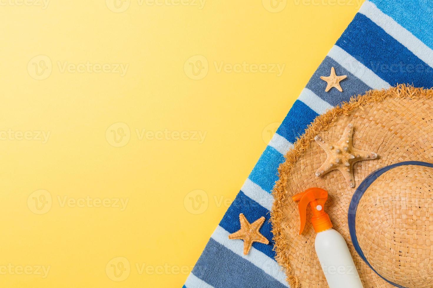 Beach flat lay accessories with copy space. Striped blue and white towel, seashells, staw sunhat and a bottle of sunblock on yellow background. Summer holiday concept photo