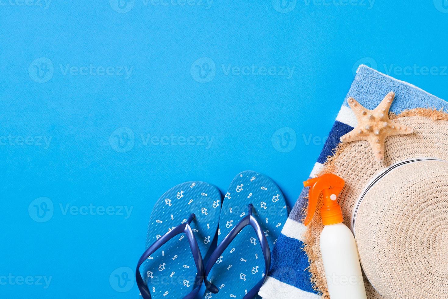 Summer beach flat lay accessories. Sunscreen bottle cream, straw hat, flip flops, towel and seashells on colored Background. Travel holiday concept with copy space photo