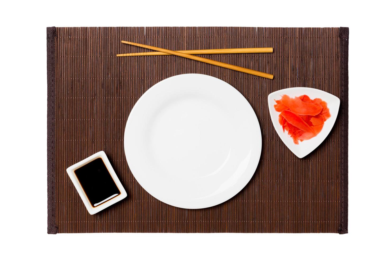 Empty round white plate with chopsticks for sushi, ginger and soy sauce on dark bamboo mat background. Top view with copy space for you design photo